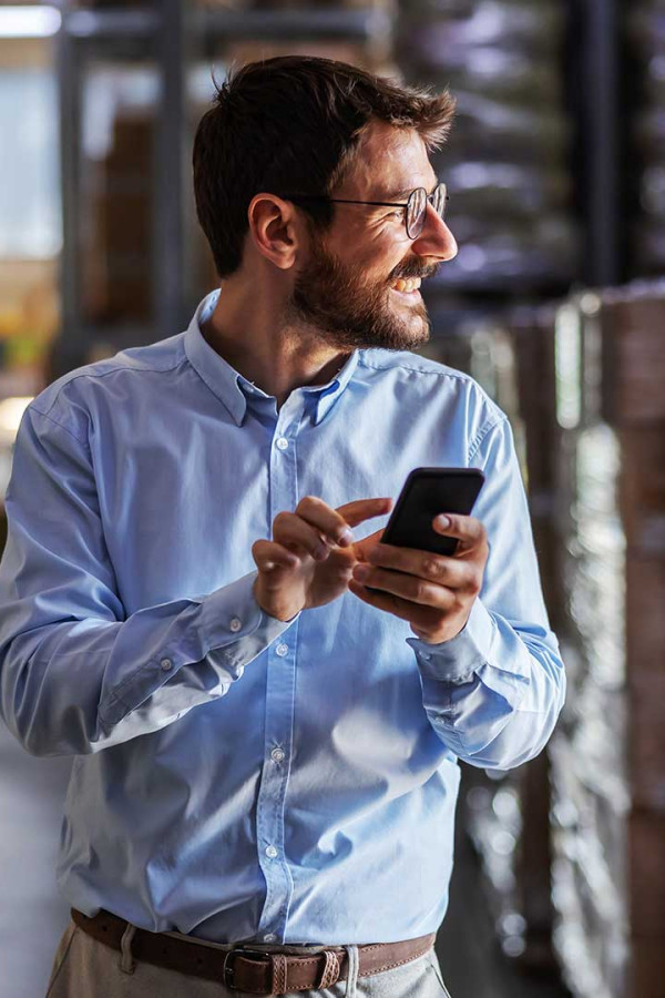 Man in warehouse smiling holding cell phone.